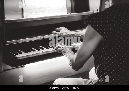 Old woman playing pipe organ in church. Black and white rear view of musician hands on keyboards. Stock Photo