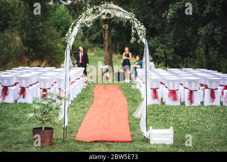 Wedding decoration - arch, carpet and decorated chairs on lawn in park. Outdoor nuptials. Wedding day concept. Stock Photo