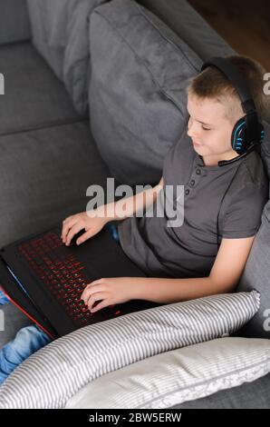 Child in headphones playing online video game on laptop computer at home. Technology concept, gaming or education. Happy boy sitting and use pc. Stock Photo