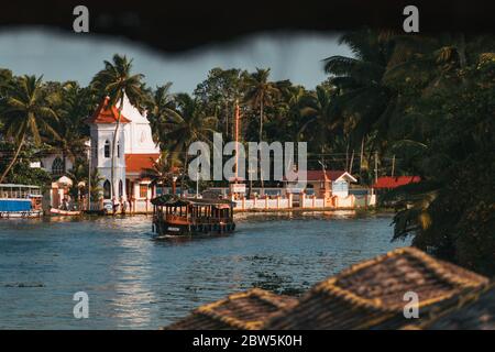 A houseboat drifts past a small Christian church on the banks of the Kerala backwaters in India Stock Photo