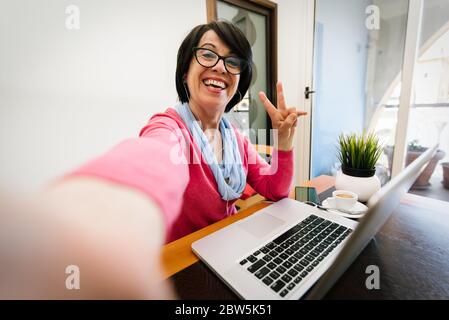 Mature older woman taking a selfie at home using computer technology. Stock Photo
