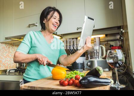 Senior woman cooking at home using digital tablet Stock Photo