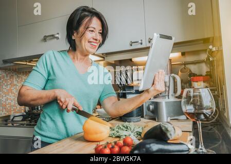 Senior woman cooking at home using digital tablet Stock Photo