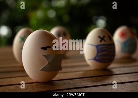 Funny eggs with human faces. Eggs wearing face masks or chinstraps. Selective focus. Colored chinstraps on white eggs. Stock Photo