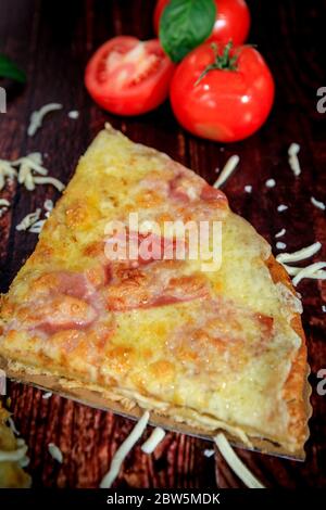 Top view of homemade ham, salami and cheese pizza slice on wooden background Stock Photo