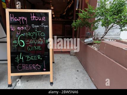 a sidewalk blackboard sign in front of a pub offers happy hour to go with a list of drinks during the coronavirus or covid-19 pandemic Stock Photo