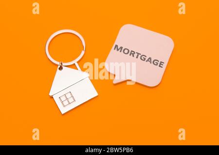 Mortgage concept. Metal keychain in the form of a house and a sticker with the inscription - mortgage on an orange background. Stock Photo