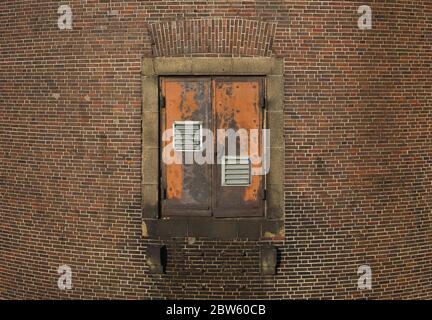 Old orange rusty metal door surrounded by a brick wall. Under the door is darker due to being damp from water. Stock Photo