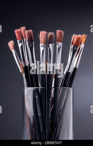 Black brushes inside a glass container against a grey background Stock Photo