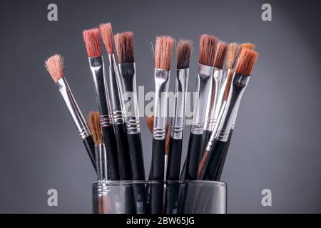 Black brushes inside a glass container against a grey background Stock Photo