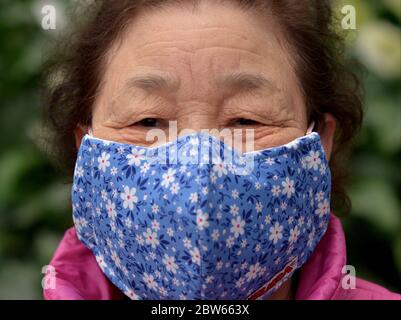 Elderly Vietnamese woman wears a washable and reusable protective cloth face mask during the 2019/20 corona-virus pandemic. Stock Photo
