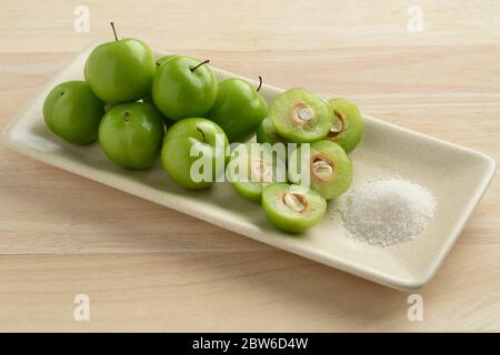 Dish with fresh green whole and half Can Erik plums and a bowl with salt Stock Photo