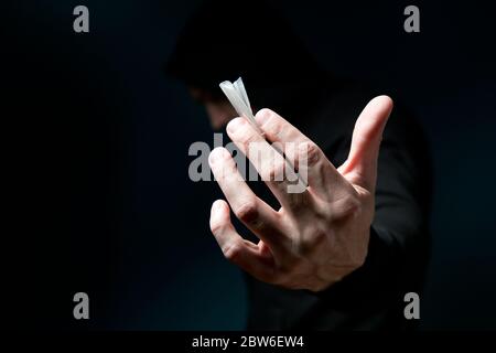 dark silhouette of a man holds out his hand a frame with a dose of the drug in the package. Stock Photo