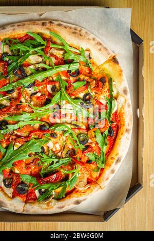 Vegetarian pizza in flat lay.Delicious Italian cuisine.Arugula,black olives,dried tomatoes & white champignon mushrooms baked in oven on crusty bread. Stock Photo