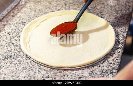 Raw dough for pizzas in kitchen.Chef cook put tomato sauce on uncooked pizza Stock Photo
