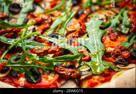 Fast food delivery.Italian pizza with arugula,black olives,dried tomatoes on crusty bread.Delicious fastfood cooked with natural ingredients for lunch Stock Photo