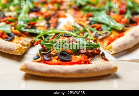 Fast food delivery.Arugula pizza with black olives,dried tomatoes & mushrooms delivered in cardboard box.Delicious Italian lunch in close up.Natural v Stock Photo