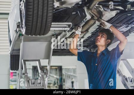 Asian mechanic repairing and light up under the car in maintainance service center which is a part of showroom, technician or engineer professional wo Stock Photo