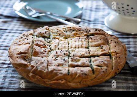 Healthy greek food concept. Whole spinach pie with sesame seeds or greek spanakopita with phyllo on kitchen table background. Stock Photo