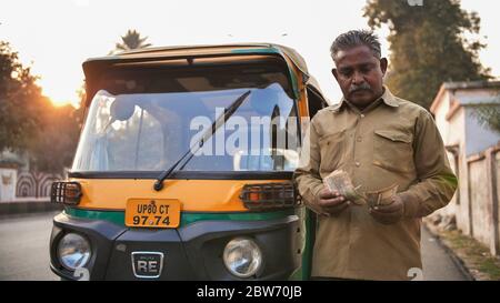 Agra, India - December 12, 2018: Indian auto rickshaw tut-tuk driver man recounts money. Stock Photo