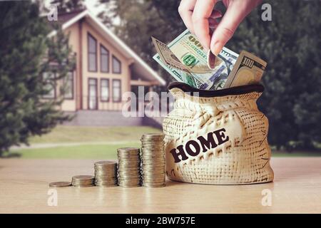 Hand put coin in Bag US dollar bills, coins Stack on table, blur background with house. Concept saving money for a home. Investment ideas, financial m Stock Photo
