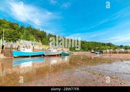 St. Martins, NB, Canada - August 3, 2019: Fishing boats rest in the mud at low tide. The Bay of Fundy has some of the highest tides in the world, the Stock Photo