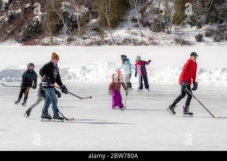 Saint John, NB, Canada - March 9, 2019: Adults and children practice outdoor ice hockey on a frozen lake. Stock Photo