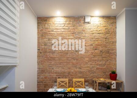 Modern loft interior of kitchen in apartment. Brick wall. Serving table and chairs. Wooden shelves with flowers. Stock Photo