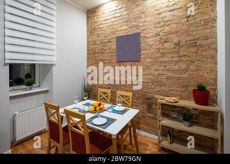 Modern loft interior of kitchen in apartment. Brick wall. Serving table and chairs. Wooden shelves with flowers. Stock Photo