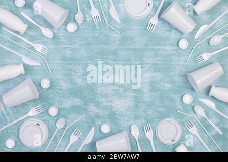 Disposable white single use plastic objects such as bottles, cups, forks and spoons on blue background Stock Photo