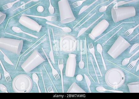 Disposable white single use plastic objects such as bottles, cups, forks and spoons on blue background Stock Photo