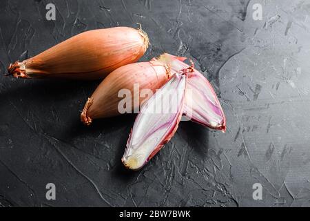 Shallot, eschalot or scallion raw ripe onions sliced and halved black concrete textured background top view space for text. Stock Photo