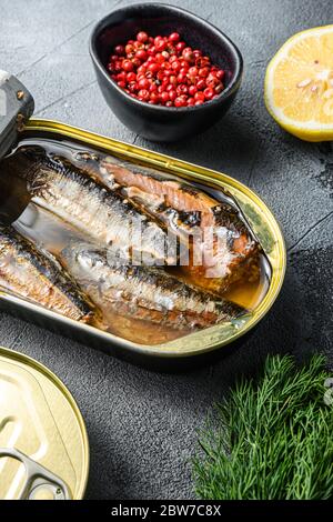 Canned saury, open and closed can with wfresh herbs, peppercorns, lemon, on grey concrete stone background side view close up. Stock Photo