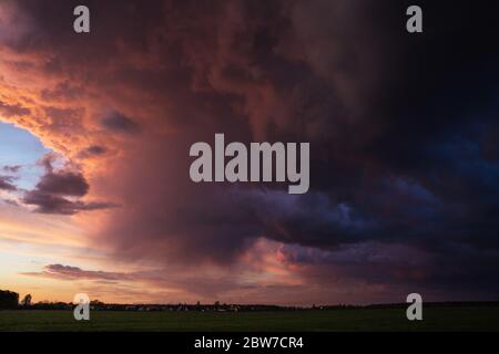 Colorful dramatic red sky with fluffy clouds at sunset before before a thunderstorm and rain with the spacious field Stock Photo