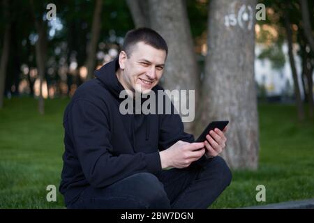Man reading electronic book handsome guy read e-book tablet sitting public park summer day Caucasian male holding ebook in hand looking device screen Stock Photo
