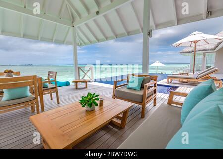 Luxury swimming pool near beach front, view from over water wooden terrace. Amazing tropical villa, loungers and chairs with umbrellas and sofa Stock Photo