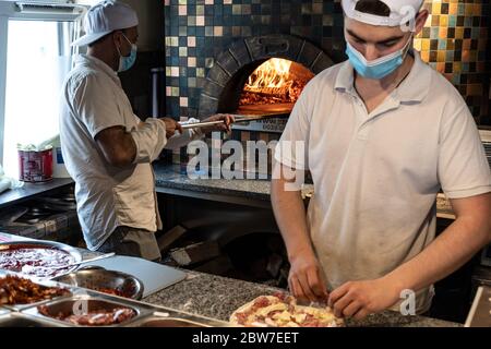 Chefs preparing pizza in a pizzeria wearing masks and protections during covid or coronavirus emergency, reopening pizzerias and restaurants Stock Photo