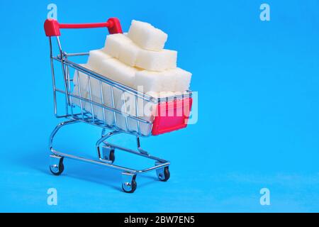 Shopping cart is filled with refined sugar cubes on a blue background Stock Photo