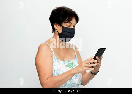brazilian senior woman using smartphone wearing mask Stock Photo