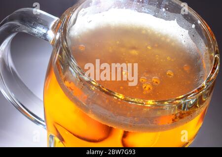 Illuminated mug full of beer with bubbles in light foam on grey background. Stock Photo