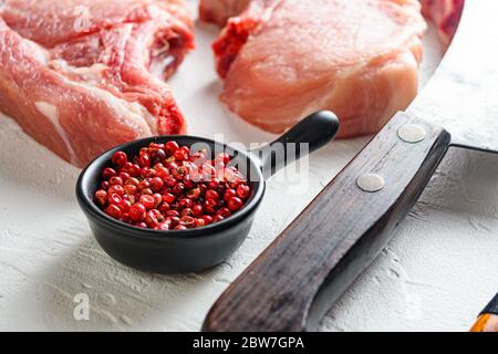 Rose peppercorns in black ceramic bowl overFresh organic raw pork meat set for grilling, baking or frying and ingredients for cooking on white surface Stock Photo
