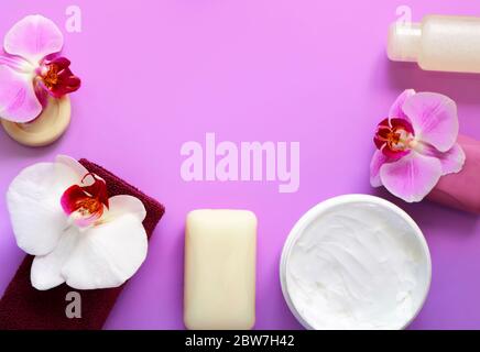 Soap, towel, cream and hygiene product, decorated with white and lilac orchid flowers on a lilac background. Spa concept Stock Photo
