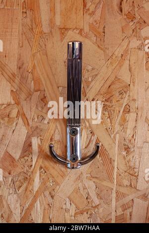 Nickel-plated hook for clothes attached to the OSB panel. Pressed wood shavings with hook attached with black screws. Vertical. Stock Photo