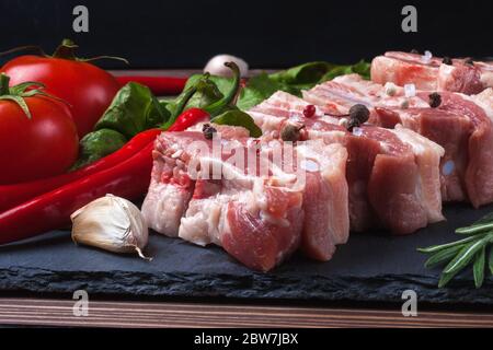 Raw slices of pork on a black slate board, tomatoes, red pepper and powder. Pork belly with vegetables. High quality photo Stock Photo