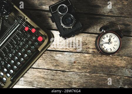 Old retro typewriter, alarm clock and camera on a wooden background top view Stock Photo
