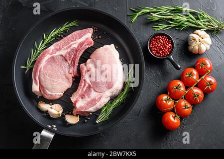 Raw Pork Loin chops in skillet near ingredients wtih herbs pepper and tomatoes top view. Stock Photo