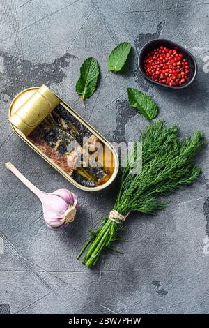 Sardinops in oil in preserve canned food, open can jar woth herbs and garlic ocer grey background top view. Stock Photo
