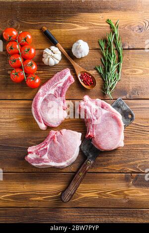 Raw pork meat chopes with herbs and spices with meat american cleaver on wooden background. Stock Photo