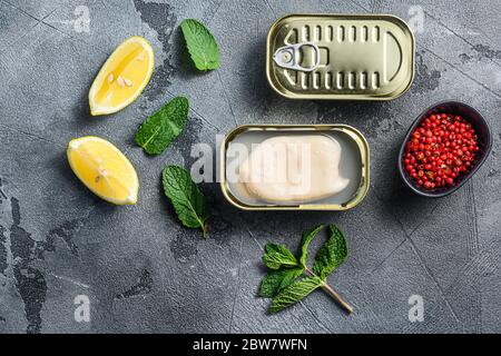 canned squid, set of opened cans closed conserve with fresh leaves and lemon with rose pepper over grey background top view . Stock Photo