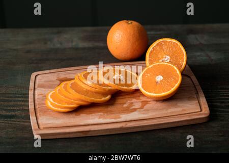 Group of fresh orange slices and halves of the fruits on wooden chopping board on the kitchen table cut by housewife for eating Stock Photo